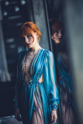 Blue chiffon gown with deep V neckline, long sheer sleeves, and high slit.